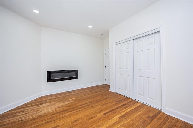 unfurnished bedroom with a glass covered fireplace, recessed lighting, wood finished floors, and baseboards