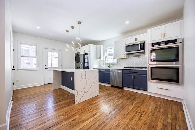 kitchen featuring stacked washer and dryer, decorative backsplash, wood finished floors, stainless steel appliances, and blue cabinets