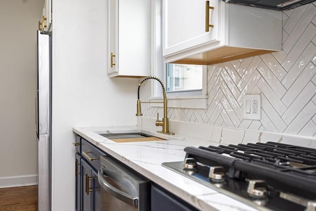 kitchen with light stone countertops, a sink, appliances with stainless steel finishes, white cabinetry, and backsplash