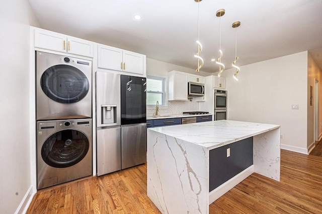 kitchen featuring stacked washer / dryer, a center island, appliances with stainless steel finishes, light wood-style floors, and white cabinetry