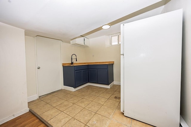 kitchen with a sink, baseboards, butcher block countertops, and freestanding refrigerator