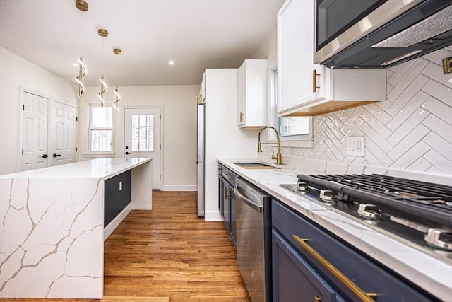 kitchen with tasteful backsplash, light stone countertops, appliances with stainless steel finishes, blue cabinets, and a sink