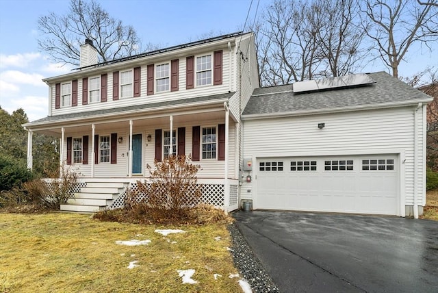 colonial home featuring a garage, covered porch, a front yard, and solar panels