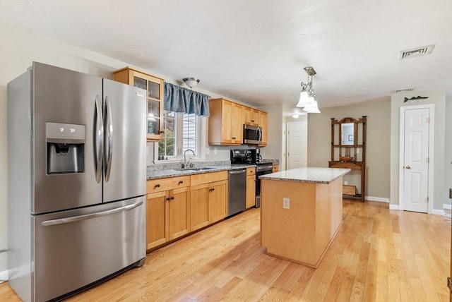 kitchen featuring appliances with stainless steel finishes, sink, a center island, light stone counters, and light wood-type flooring