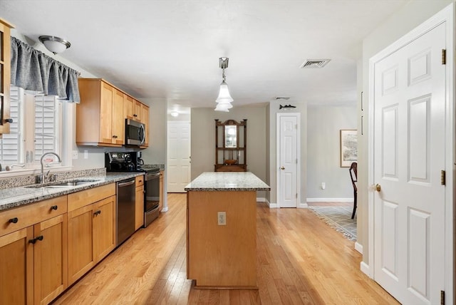 kitchen featuring sink, hanging light fixtures, appliances with stainless steel finishes, a kitchen island, and light stone countertops