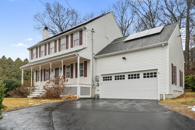 colonial home with a garage, solar panels, and a porch