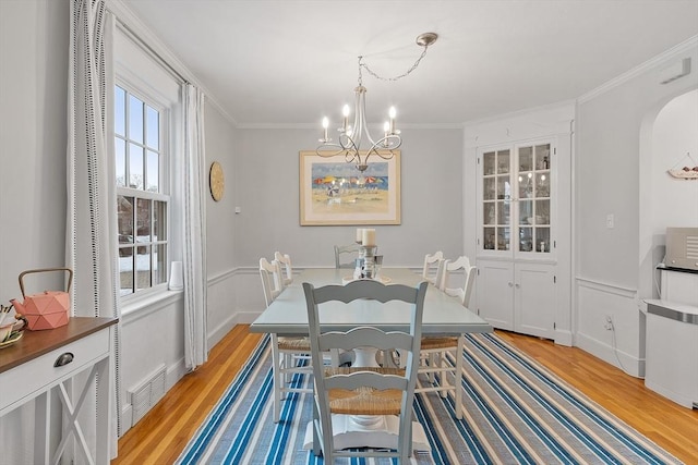 dining space featuring visible vents, arched walkways, ornamental molding, an inviting chandelier, and light wood-style floors