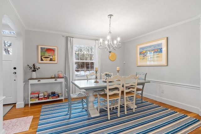 dining space with baseboards, ornamental molding, wood finished floors, and a notable chandelier