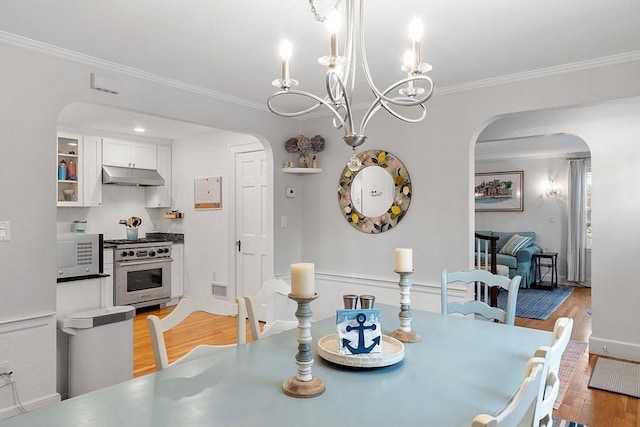 dining room with light wood-style floors, baseboards, arched walkways, and ornamental molding