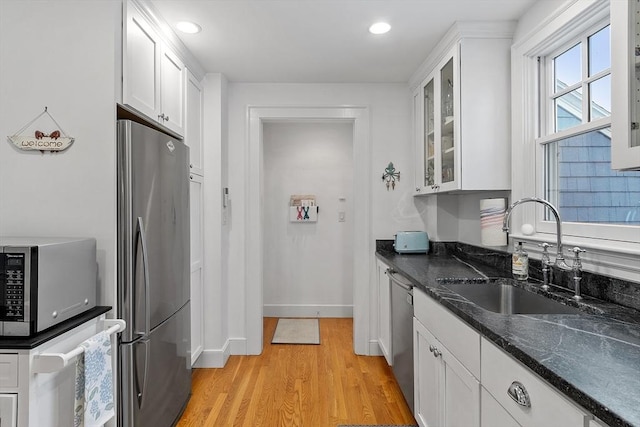 kitchen featuring stainless steel appliances, a sink, white cabinets, light wood finished floors, and glass insert cabinets