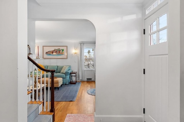 entryway featuring arched walkways, light wood finished floors, visible vents, baseboards, and stairs