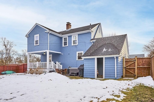 snow covered property with roof with shingles, a chimney, fence, and a gate