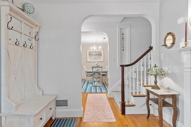 interior space featuring arched walkways, a notable chandelier, light wood finished floors, visible vents, and baseboards