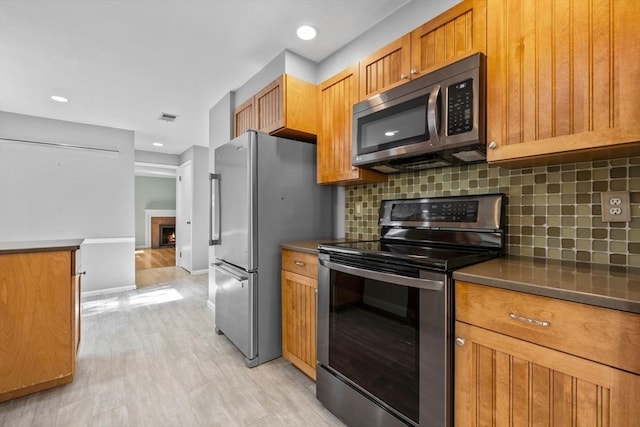 43 Grove Hill Park, Newton, MA 02460 - kitchen featuring appliances with stainless steel finishes, tasteful backsplash, light wood-style flooring, brown cabinetry, and dark countertops