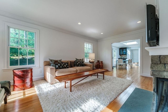 living room featuring crown molding, light wood-style floors, a stone fireplace, recessed lighting, and baseboards