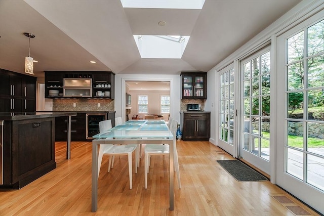 dining area featuring visible vents, a fireplace, lofted ceiling with skylight, wine cooler, and light wood-style flooring