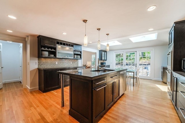 kitchen featuring a skylight, dark countertops, dark brown cabinets, a sink, and dishwasher