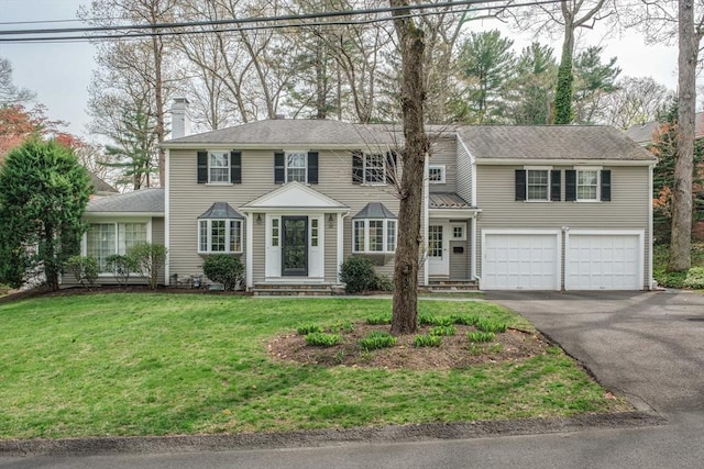 colonial inspired home with a garage, a front yard, entry steps, a chimney, and driveway
