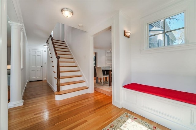 staircase with baseboards, ornamental molding, decorative columns, and wood finished floors