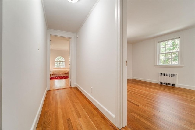 corridor featuring crown molding, a healthy amount of sunlight, light wood-style flooring, and radiator