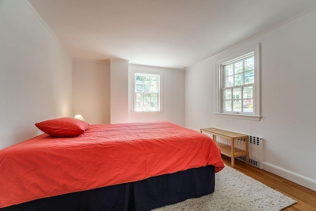 bedroom with radiator heating unit, baseboards, ornamental molding, and wood finished floors