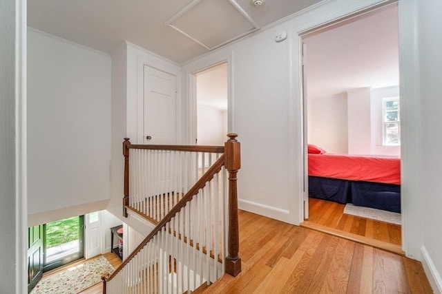 corridor featuring attic access, light wood finished floors, a wealth of natural light, and an upstairs landing