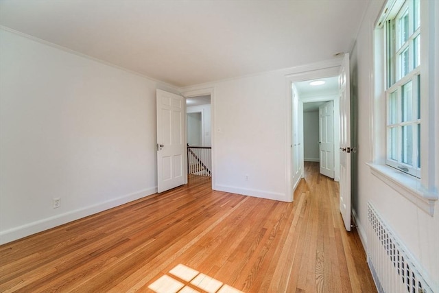 spare room featuring baseboards, light wood-style flooring, and radiator