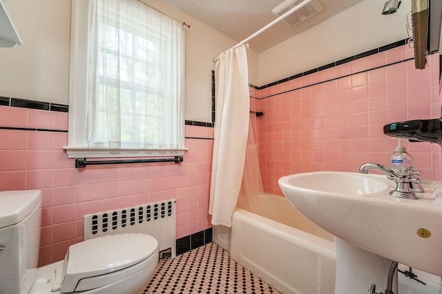 bathroom with a sink, toilet, radiator heating unit, tile walls, and shower / tub combo