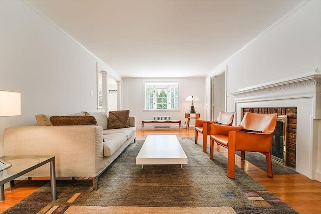 living area with a brick fireplace, wood finished floors, and radiator