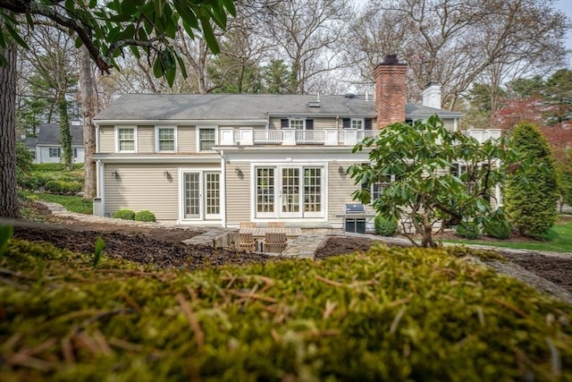 back of property with french doors, a chimney, a patio area, and a balcony
