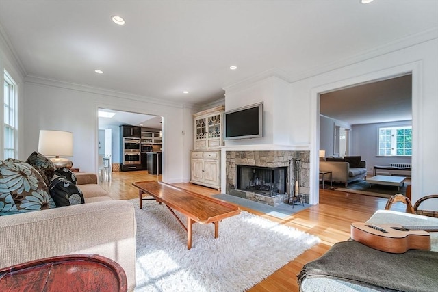 living area with crown molding, a fireplace, recessed lighting, and light wood-style flooring