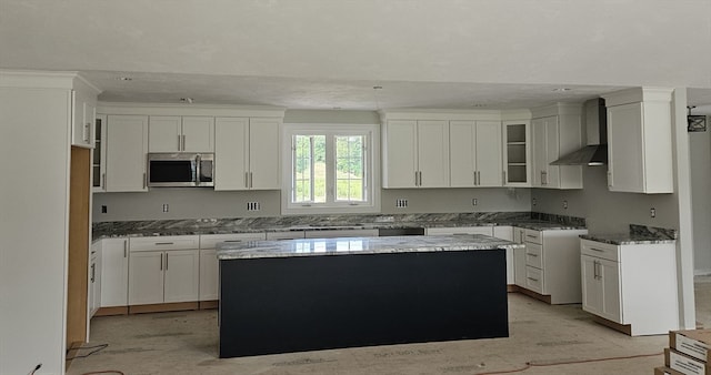 kitchen featuring white cabinets, wall chimney exhaust hood, dark stone counters, and a center island