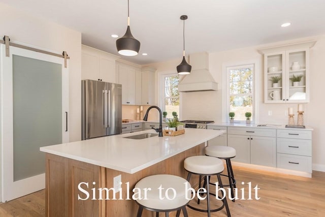 kitchen with light wood finished floors, custom exhaust hood, freestanding refrigerator, a sink, and light countertops