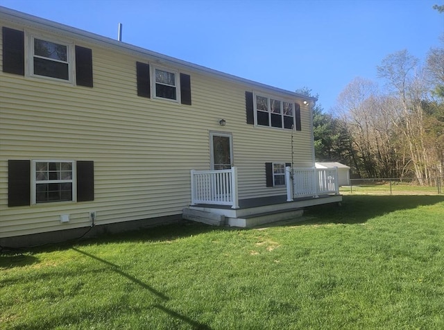rear view of house featuring a wooden deck, a yard, and fence