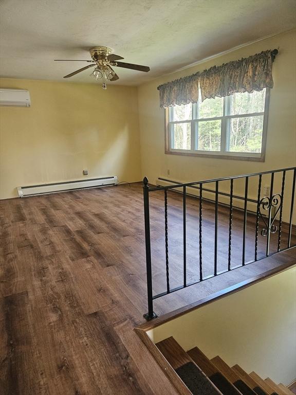 empty room featuring ceiling fan, a wall mounted air conditioner, wood finished floors, a baseboard radiator, and a baseboard heating unit