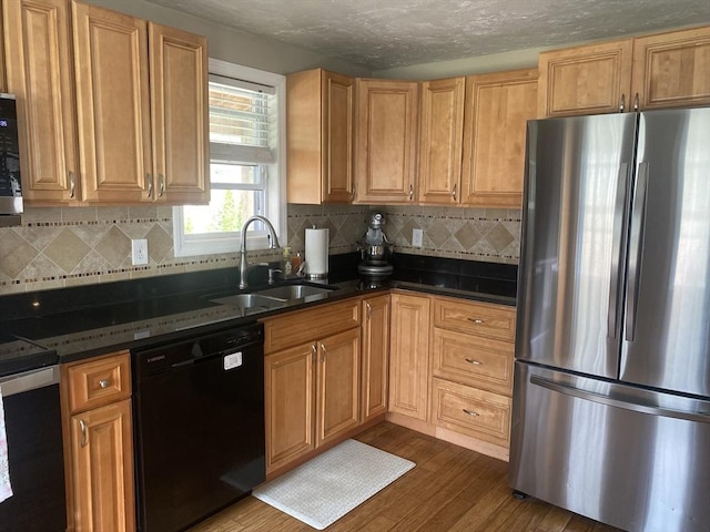 kitchen featuring dark stone countertops, tasteful backsplash, a sink, dark wood finished floors, and stainless steel appliances