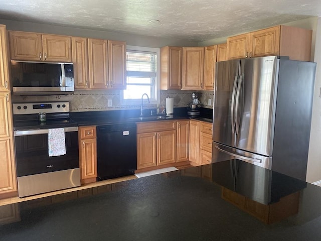kitchen with dark countertops, a textured ceiling, tasteful backsplash, a sink, and appliances with stainless steel finishes