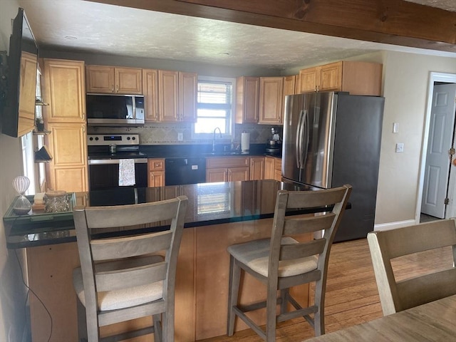 kitchen featuring decorative backsplash, a breakfast bar area, dark countertops, a sink, and stainless steel appliances