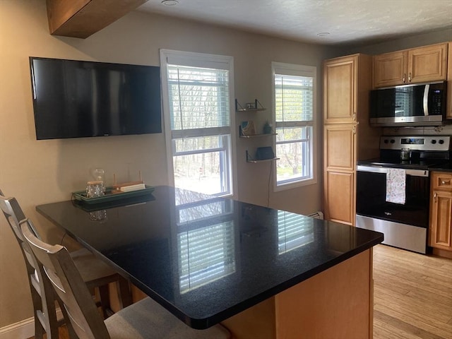 kitchen with a peninsula, light wood-style flooring, appliances with stainless steel finishes, and a kitchen breakfast bar