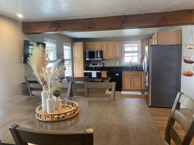 kitchen featuring dark countertops, appliances with stainless steel finishes, a sink, light wood-style floors, and beamed ceiling
