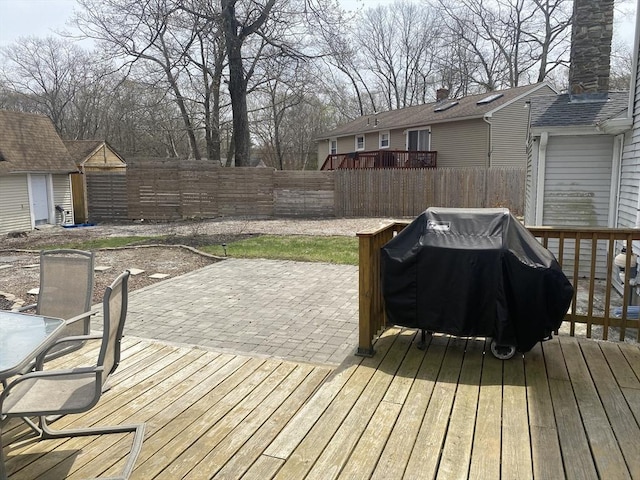 wooden deck with outdoor dining space, area for grilling, a fenced backyard, an outbuilding, and a patio