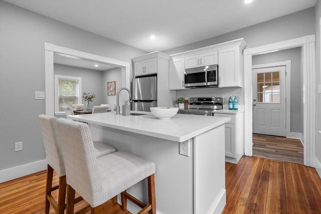 kitchen featuring stainless steel appliances, white cabinets, wood finished floors, light countertops, and a breakfast bar