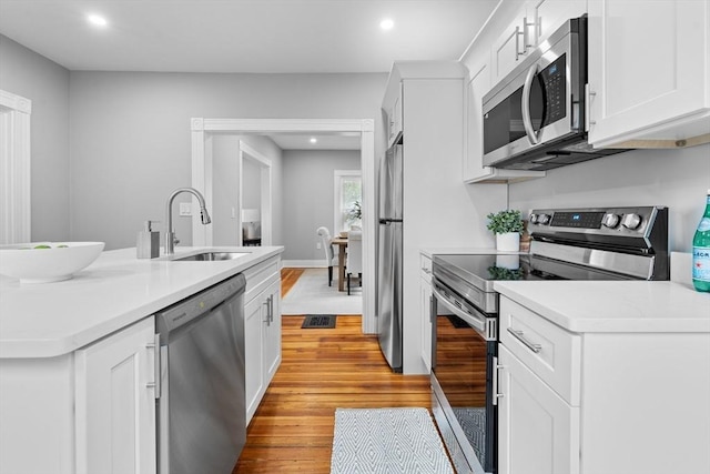 kitchen with stainless steel appliances, a sink, light wood finished floors, white cabinetry, and recessed lighting
