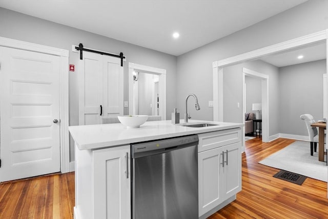 kitchen featuring dishwasher, a sink, a barn door, light countertops, and wood finished floors