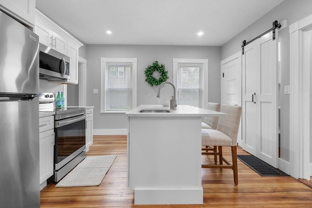 kitchen featuring stainless steel appliances, a sink, a barn door, light wood finished floors, and white cabinetry