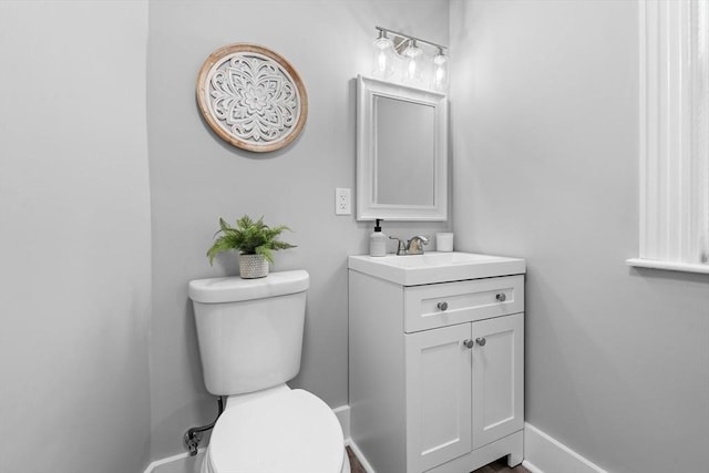 half bathroom featuring toilet, vanity, and baseboards