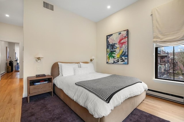 bedroom with wood finished floors, recessed lighting, and a baseboard heating unit