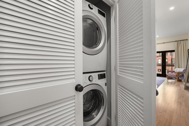 laundry area featuring stacked washer / dryer, wood finished floors, and recessed lighting