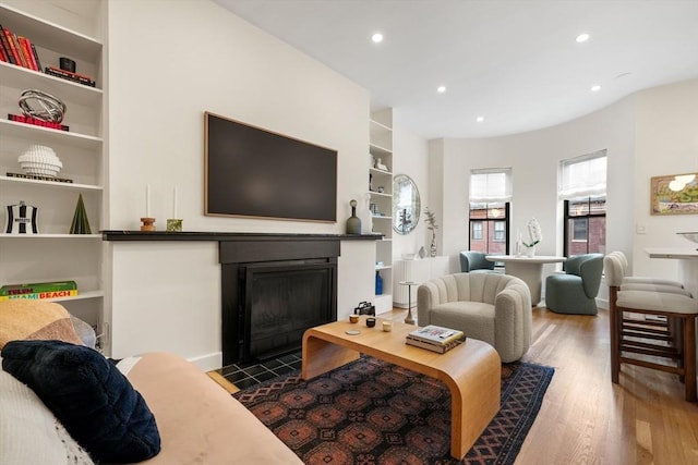 living room with built in features, a fireplace with flush hearth, wood finished floors, and recessed lighting