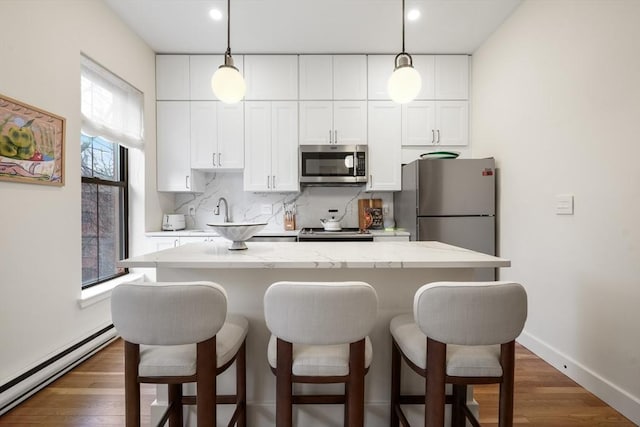 kitchen with appliances with stainless steel finishes, a baseboard heating unit, a breakfast bar area, white cabinetry, and decorative backsplash
